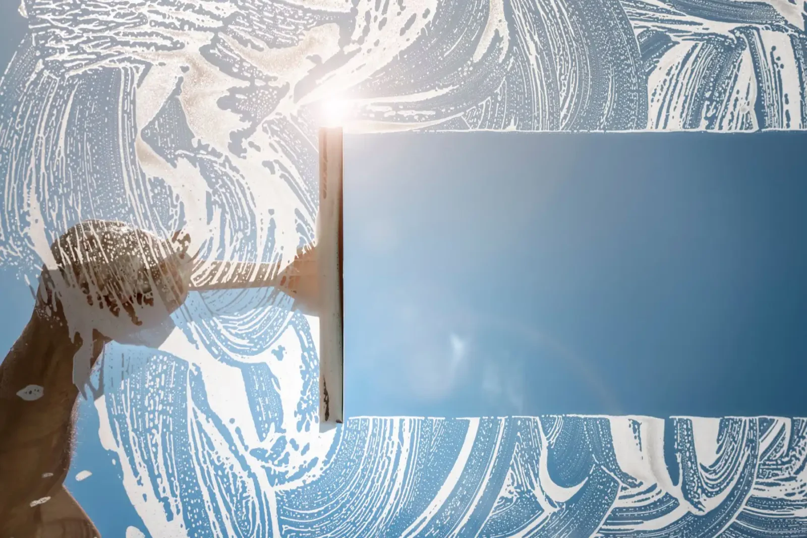 Raamwisser trekt een strook zeepsop van een raam, met blauwe lucht erachter